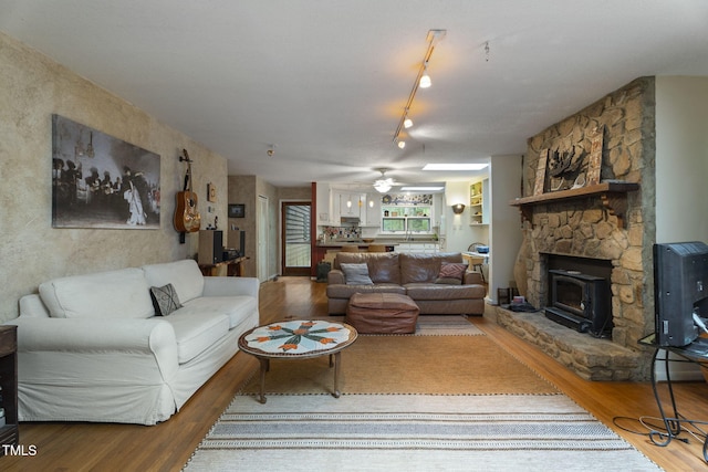 living room featuring wood finished floors, a wood stove, and a ceiling fan