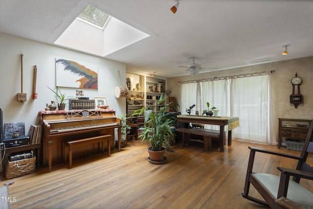 living area with ceiling fan, a skylight, hardwood / wood-style flooring, and a textured ceiling
