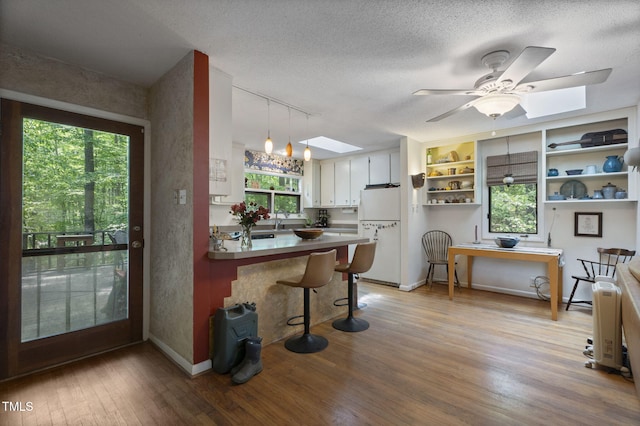 kitchen with a skylight, freestanding refrigerator, open shelves, a peninsula, and wood finished floors