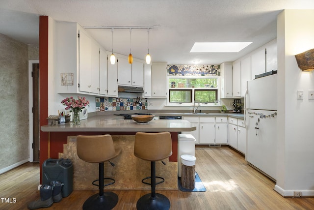 kitchen with freestanding refrigerator, a peninsula, light wood-style flooring, and a skylight