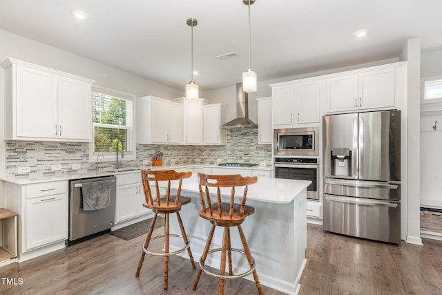 kitchen with light countertops, wall chimney exhaust hood, a center island, stainless steel appliances, and tasteful backsplash
