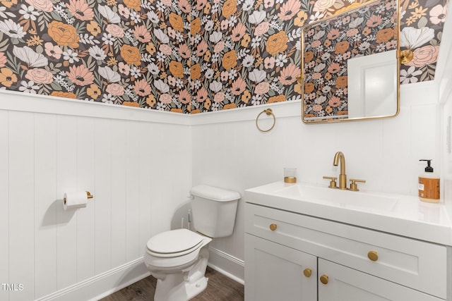 bathroom featuring wood finished floors, baseboards, vanity, toilet, and wallpapered walls