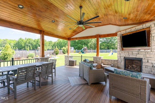 deck with an outdoor living space with a fireplace, outdoor dining space, a playground, a fenced backyard, and a lawn