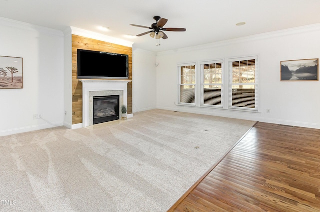 unfurnished living room featuring ornamental molding, baseboards, a ceiling fan, a glass covered fireplace, and wood finished floors