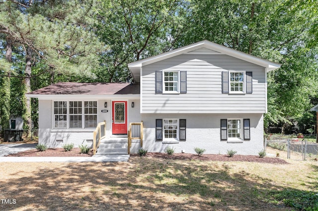 split level home with fence, roof with shingles, and brick siding