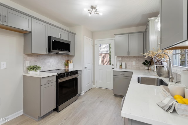 kitchen with light wood finished floors, electric range oven, stainless steel microwave, a wealth of natural light, and gray cabinetry