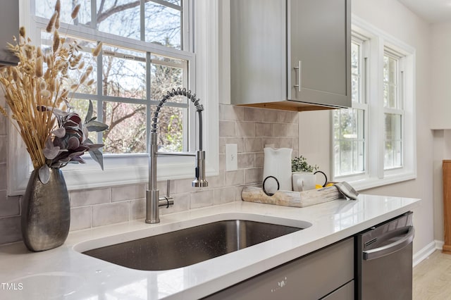 kitchen with a sink, gray cabinets, backsplash, and dishwasher
