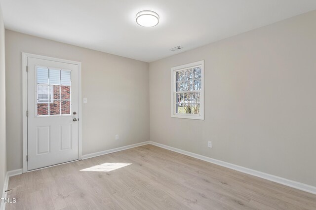 empty room with baseboards, visible vents, and light wood finished floors