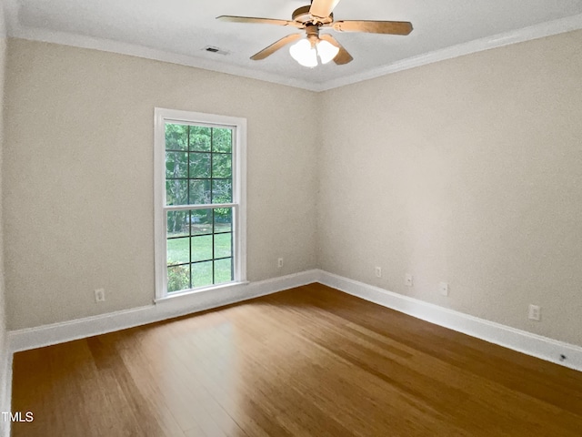 spare room featuring crown molding, dark wood-type flooring, a healthy amount of sunlight, and visible vents
