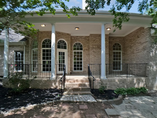 view of exterior entry with a porch and brick siding