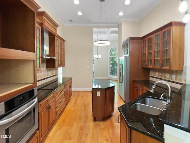 kitchen featuring a kitchen island, brown cabinets, a sink, stainless steel appliances, and wall chimney exhaust hood