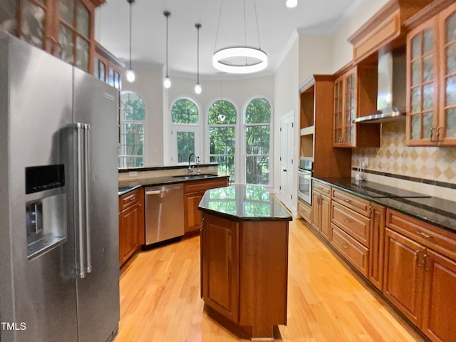 kitchen with brown cabinetry, wall chimney range hood, a center island, a sink, and appliances with stainless steel finishes