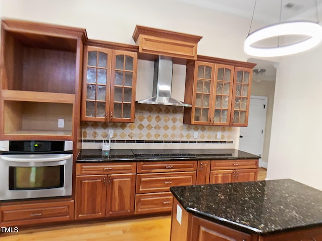 kitchen featuring wall chimney range hood, oven, black electric cooktop, dark stone counters, and decorative backsplash