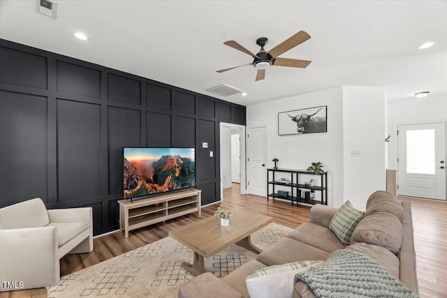 living area featuring a decorative wall, light wood-style flooring, a ceiling fan, and recessed lighting