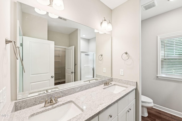 full bath featuring a shower stall, toilet, wood finished floors, double vanity, and baseboards