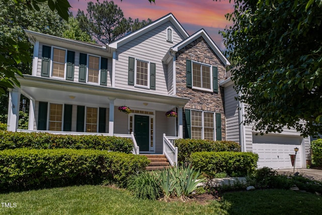 view of front of property featuring a porch, a garage, driveway, and stone siding