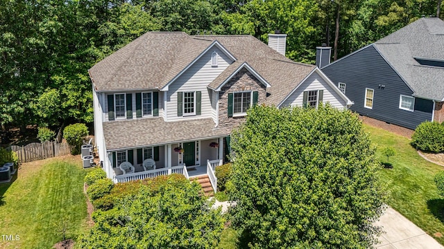 traditional home featuring covered porch, a chimney, central air condition unit, and roof with shingles