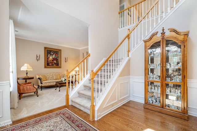 stairway with wood finished floors, wainscoting, ornamental molding, and a decorative wall
