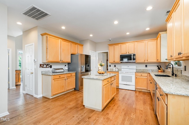 kitchen with stainless steel appliances, a sink, light brown cabinetry, light wood-type flooring, and a center island