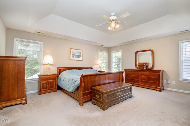 bedroom with a raised ceiling, light carpet, multiple windows, and baseboards