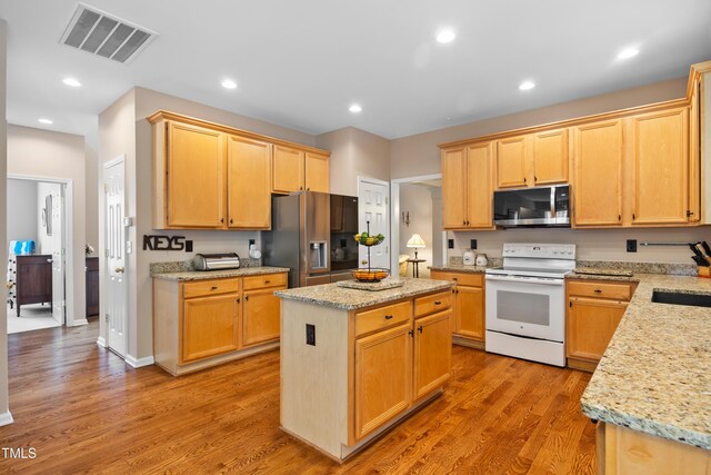 4608 Regency Dr, Durham, NC 27713 - kitchen with appliances with stainless steel finishes, a center island, light wood finished floors, light stone counters, and light brown cabinetry
