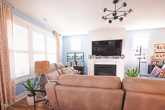 living room featuring visible vents, baseboards, a glass covered fireplace, an inviting chandelier, and dark wood-type flooring