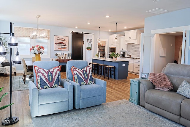 living area featuring visible vents, a barn door, light wood finished floors, an inviting chandelier, and recessed lighting