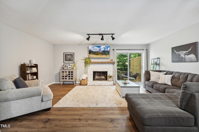 living area featuring rail lighting, dark wood-style floors, baseboards, and a stone fireplace