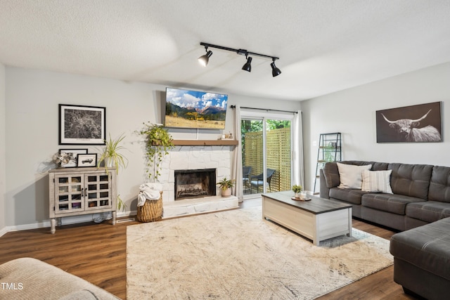 living room with track lighting, wood finished floors, a fireplace, baseboards, and a textured ceiling