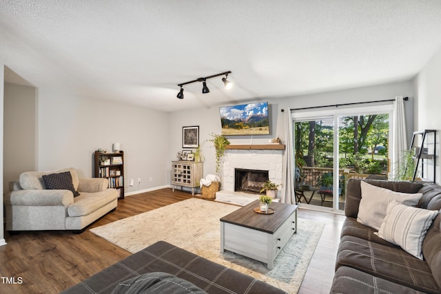 living room with track lighting, baseboards, a stone fireplace, and wood finished floors