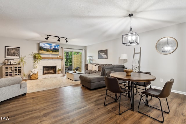 dining area with wood finished floors, a fireplace, baseboards, a textured ceiling, and rail lighting