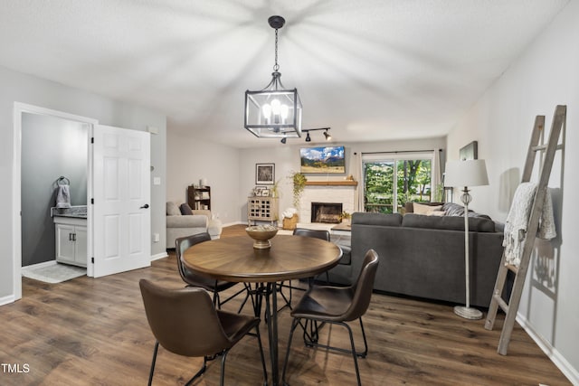 dining area featuring a stone fireplace, a chandelier, dark wood-style floors, and baseboards