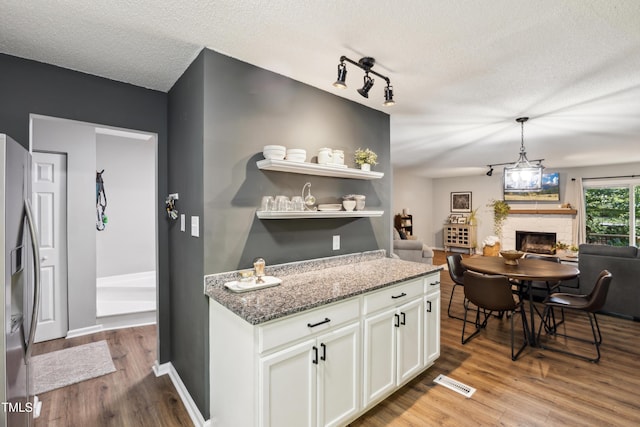 kitchen with stainless steel fridge, a fireplace, a textured ceiling, light wood-style flooring, and white cabinetry