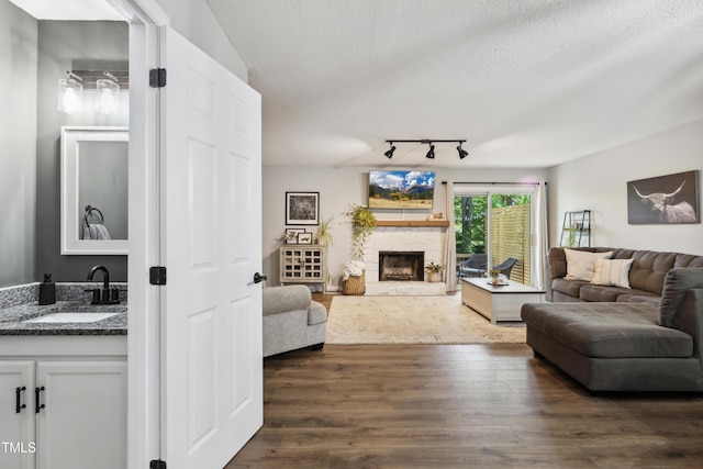 living room featuring rail lighting, a textured ceiling, dark wood-style floors, and a fireplace