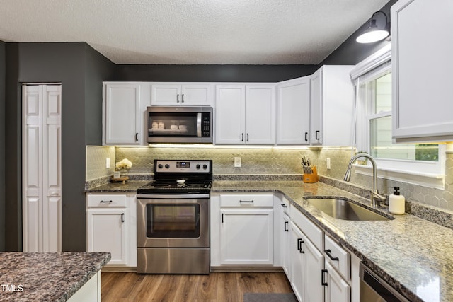 kitchen with decorative backsplash, a sink, dark stone countertops, stainless steel appliances, and white cabinetry