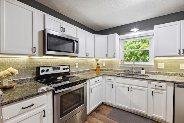 kitchen with a sink, appliances with stainless steel finishes, wood finished floors, and white cabinetry