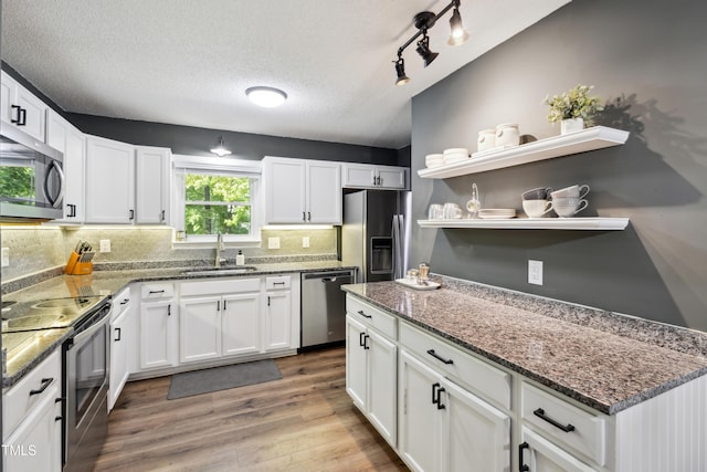 kitchen featuring white cabinetry, a sink, light wood finished floors, backsplash, and stainless steel appliances
