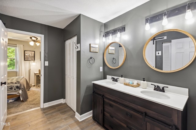 ensuite bathroom featuring a sink, baseboards, double vanity, and wood finished floors