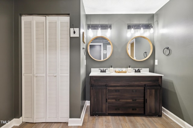 bathroom with double vanity, wood finished floors, a sink, baseboards, and a closet