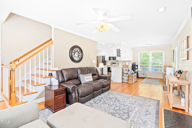 living room featuring crown molding, light wood-style flooring, stairs, a ceiling fan, and baseboards