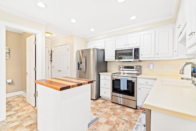 kitchen featuring white cabinetry, a sink, ornamental molding, stainless steel appliances, and butcher block countertops