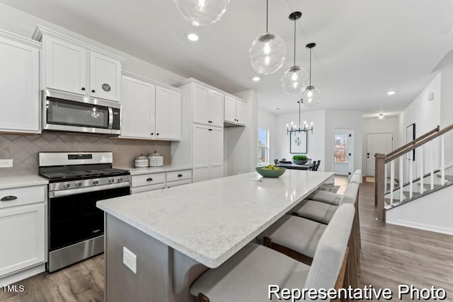 kitchen featuring decorative backsplash, recessed lighting, white cabinetry, light wood finished floors, and stainless steel appliances