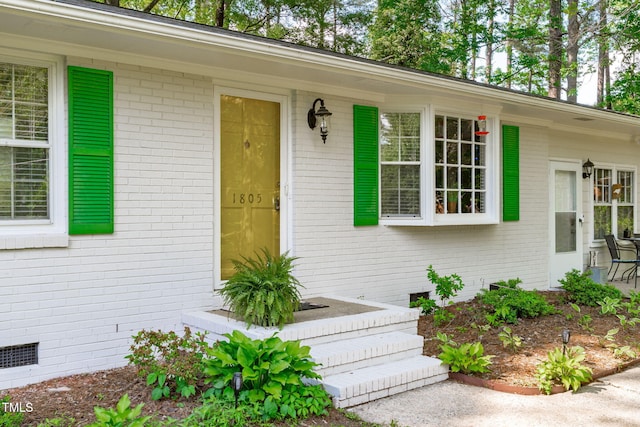 view of exterior entry featuring brick siding and crawl space