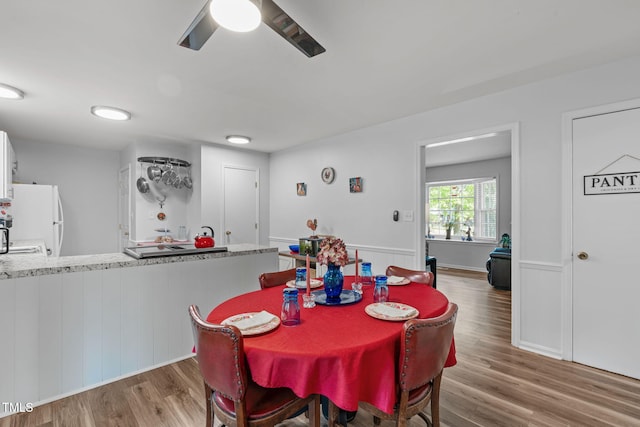 dining room with a wainscoted wall, a ceiling fan, and wood finished floors