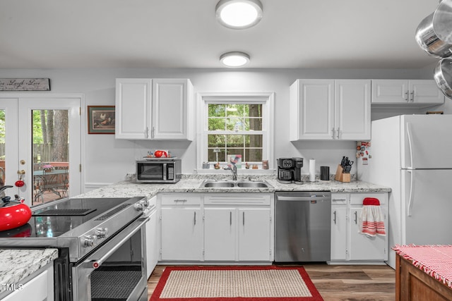 kitchen with appliances with stainless steel finishes, a sink, plenty of natural light, and white cabinetry