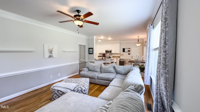 living room with baseboards, ornamental molding, a ceiling fan, and wood finished floors