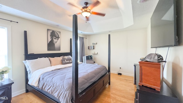 bedroom featuring baseboards, multiple windows, a tray ceiling, and light wood-style flooring