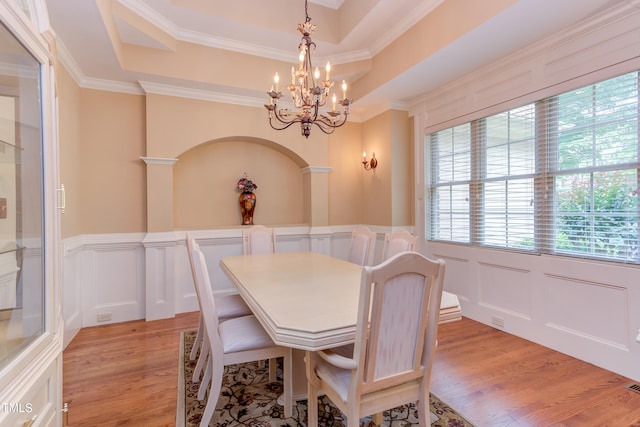 dining area featuring a decorative wall, a chandelier, light wood finished floors, a tray ceiling, and wainscoting