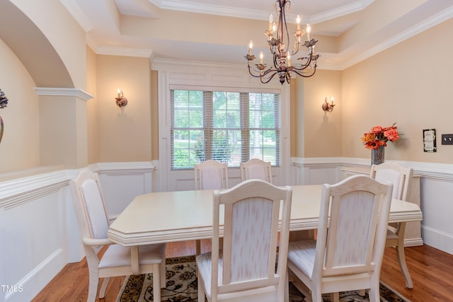 dining space featuring a decorative wall, a chandelier, crown molding, wainscoting, and wood finished floors