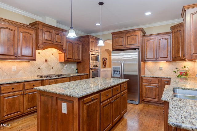 kitchen with appliances with stainless steel finishes, a sink, arched walkways, a kitchen island, and light stone countertops